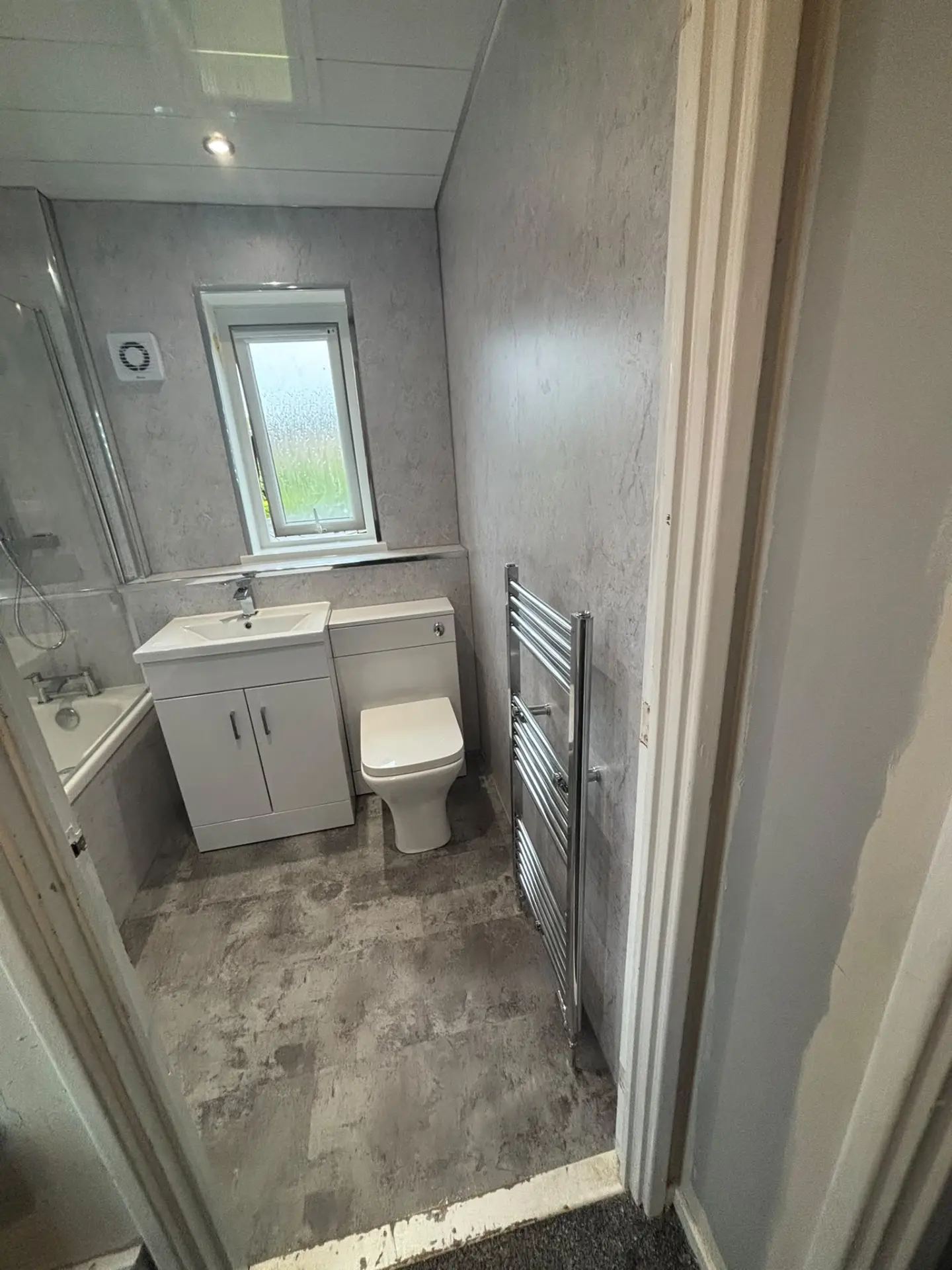 View into bathroom with shower bath, vanity, toilet and chrome heated towel rail