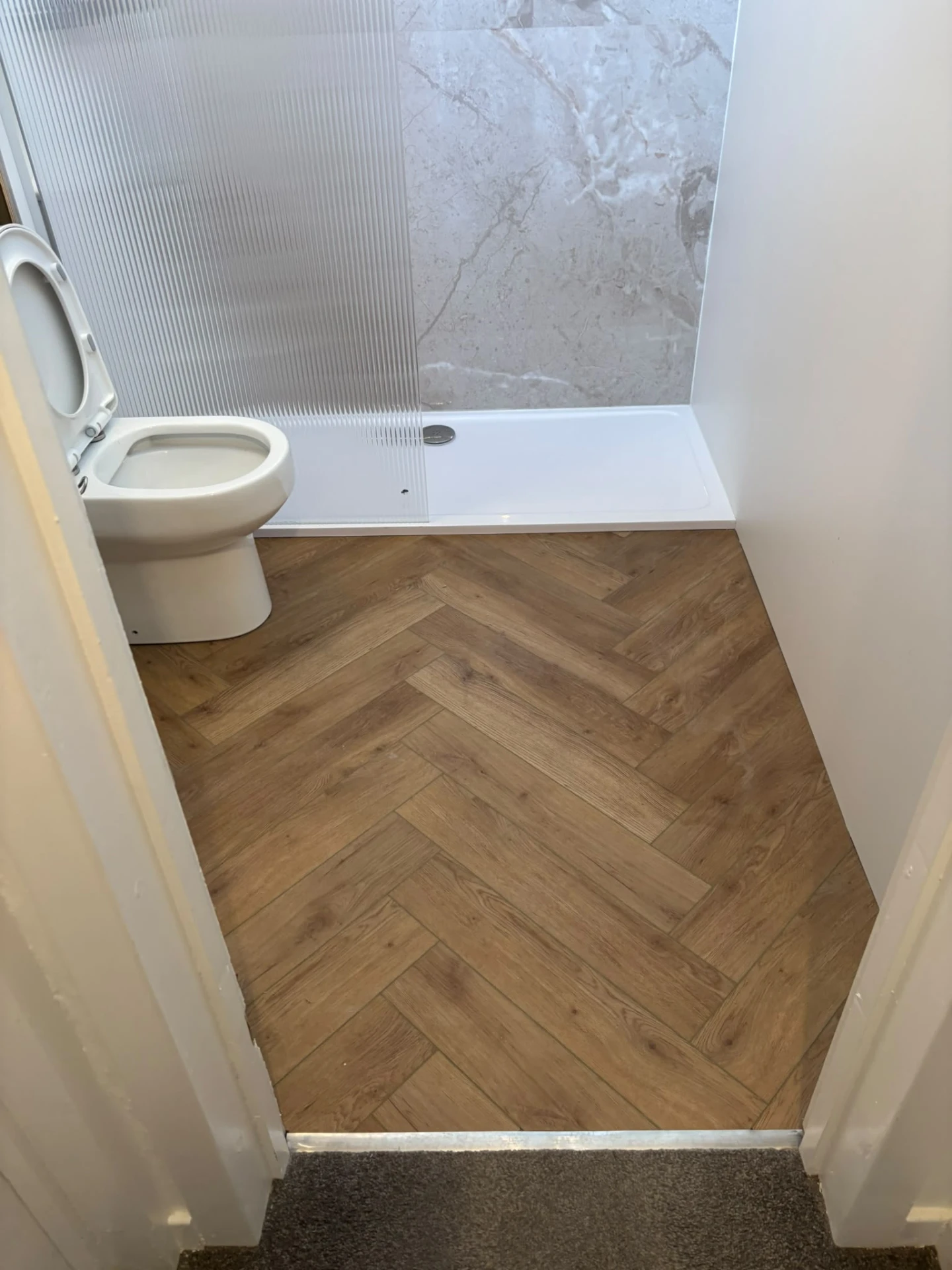 Shower room with herringbone wood-effect floor, fluted glass screen and marble-effect wall boards