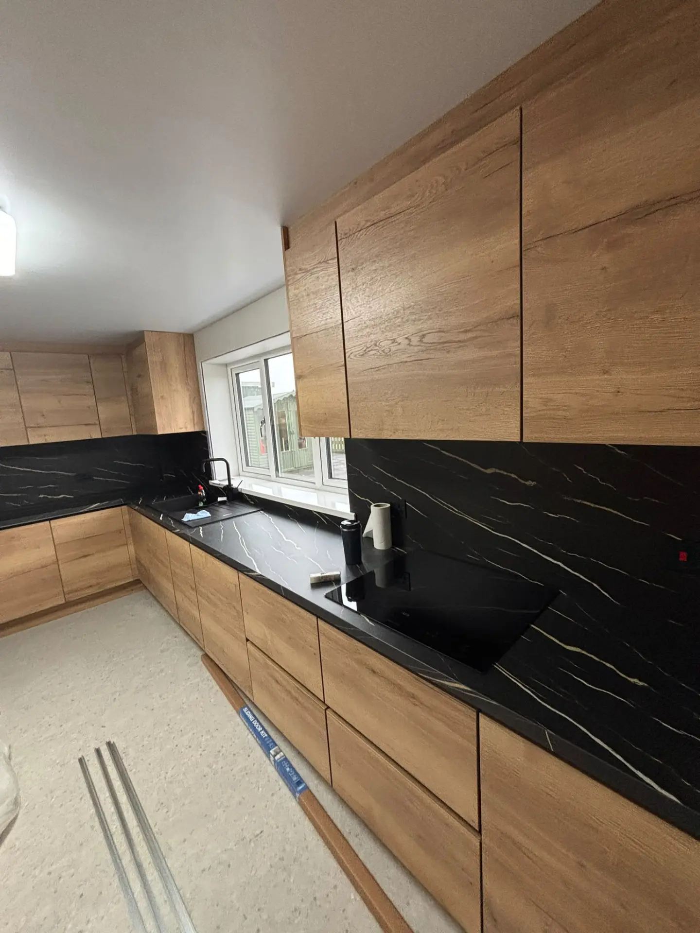 Oak-effect handleless kitchen with black marble-effect worktops and splashbacks