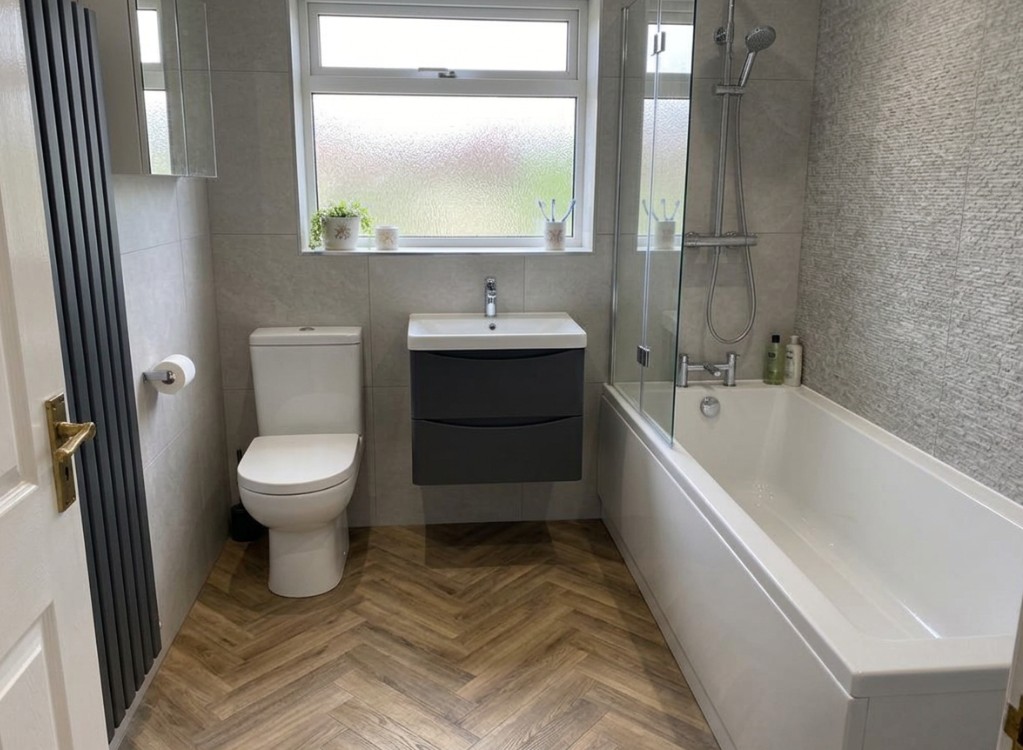 Modern bathroom with grey tile-effect wall boards, dark vanity unit and herringbone flooring after renovation