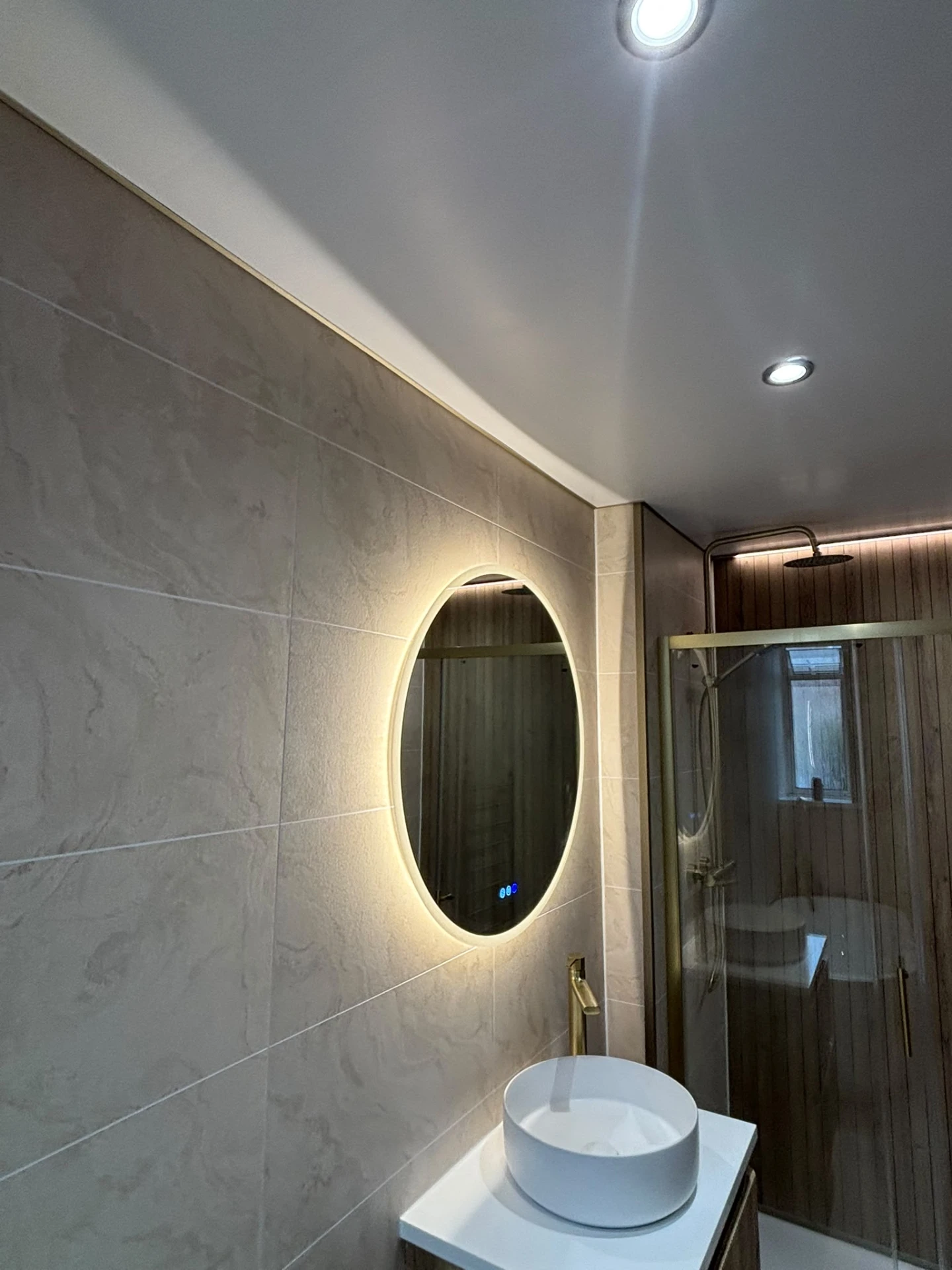 Close-up of round backlit mirror, countertop basin and walk-in shower