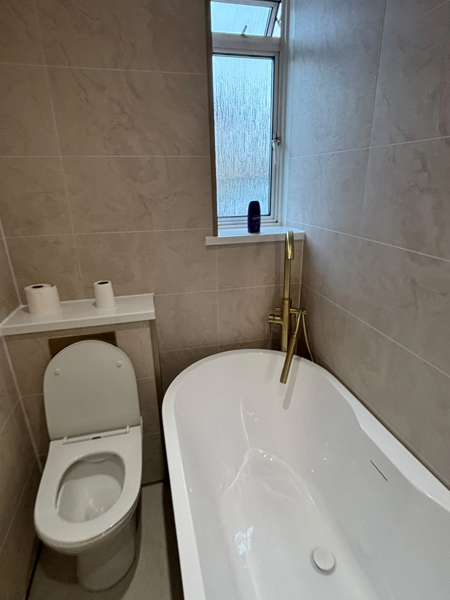 White bath with gold taps and tile-effect wall boards in a compact bathroom